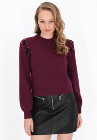 Pulover tricotat bordeaux cu mâneci lungi, având accente din dantelă neagră pe umeri și o margine ribonată, asortat cu o fustă mini din piele neagră.