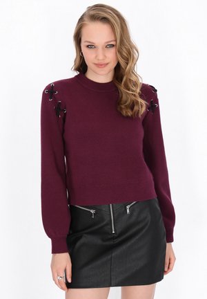 Maglione borgogna lavorato a maglia con maniche lunghe, caratterizzato da dettagli in pizzo nero sulle spalle e orlo a coste, abbinato a una mini gonna in pelle nera.
