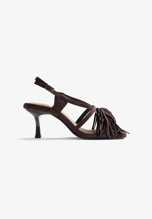Sandalia de tacón alto con tira trasera en ante marrón, detalles de flecos en las correas frontales y hebilla ajustable en el tobillo.