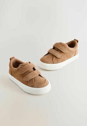 Barna művelúr tornacipő fehér gumitalppal és két állítható tépőzáras pánttal, világos háttéren bemutatva.