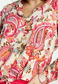 Floral blouse in lightweight cream fabric, featuring pink, orange, and blue paisley patterns, with button closures and a gathered hem.