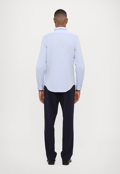 Chemise bleu clair à manches longues avec un ourlet arrondi et des poignets à boutons, assortie à un pantalon bleu marine. Texture lisse, coupe ajustée.