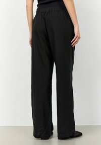 Svarta vida byxor i lätt material med elastisk midja. Tyget är något strukturerat med en avslappnad passform.