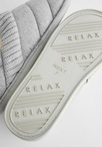 Grau stoffene Hausschuhe mit einem gesteppten Obermaterial und einer strukturierten Fußbett. Die Sohle hat erhabene "RELAX"-Buchstaben und eine glatte Oberfläche.