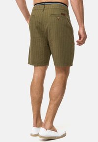 Olivenfarvede shorts med et vertikalt stribemønster, har baglommer og en kontrastfarvet talje. Kombineres med hvide sko.