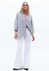 Camicia a righe con tasca, maniche ampie e vestibilità rilassata; abbinata a pantaloni bianchi a palazzo e scarpe nere.