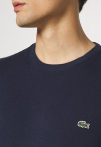 Navy blue short-sleeve t-shirt made from cotton, featuring a small green and white embroidered crocodile logo on the chest.