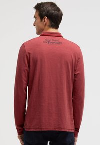 Langarmiges rotes Poloshirt mit strukturiertem Finish und einem Rückendruck, der "Camp David THE SUMMITS" liest. Verfügt über einen klassischen Kragen.
