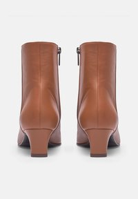 Bottines en cuir marron avec un talon courbé et une fermeture éclair à l'arrière. Texture lisse avec des coutures renforcées.