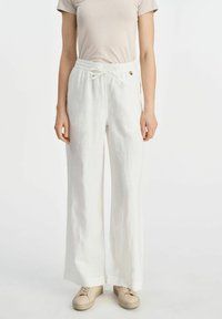 Białe lniane spodnie o szerokich nogawkach z elastycznym paskiem i sznurkiem do regulacji. Posiadają złoty guzik z przodu. Luźny krój i lekki materiał.
