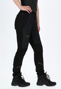 Zwarte wandelbroek met ritszakken, een slim fit en accentstiksels. Gecombineerd met stevige zwarte laarzen met een geprofileerde zool.