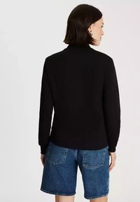 Czarny sweter z wysokim kołnierzem, długimi rękawami i prążkowanymi mankietami, w zestawie z niebieskimi szortami dżinsowymi z tylnymi kieszeniami.