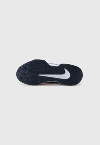 Schwarze Gummisohle eines Sneakers mit strukturiertem Zickzackmuster, versehen mit einem weißen Swoosh und lebhaften blauen und orangen Akzenten nahe der Ferse.