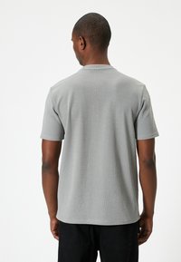 Harmaa lyhythihainen t-paita, joka on valmistettu ribbatusta kankaasta, pyöreällä kaula-aukolla ja rentolla istuvuudella. Kuvassa näkyy takanäkymä, ja paita on yksivärinen ilman kuvioita.