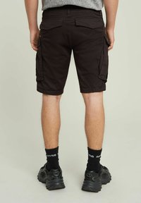 Pantaloni cargo neri con tasche laterali, risvolti e una trama liscia. Indossati con sneakers nere e calze scure.