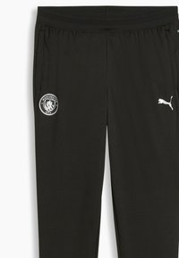 Pantaloni sportivi neri in tessuto testurizzato, con il logo del Manchester City su una gamba e il logo bianco della Puma. Vita elasticizzata per il massimo comfort.