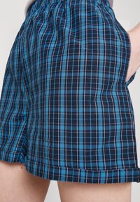 Rutiga shorts med ett blått och marinblått rutmönster, med elastisk midja och sidofickor. Materialet verkar lätt och andningsbart.