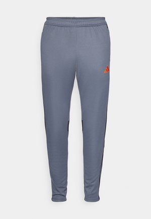 Pantalons de sport gris à coupe ajustée, avec des panneaux latéraux noirs et un logo Adidas orange sur la cuisse droite. Matériau doux et extensible.