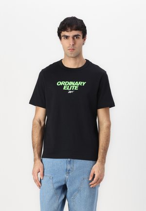 Tricou negru din bumbac cu inscriptionarea "ORDINARY ELITE" în text verde neon. Mâneci scurte, guler rotund, croială lejeră. Purtați cu blugi din denim albastri.