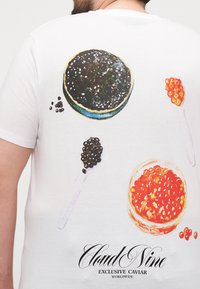 White t-shirt featuring colorful illustrations of caviar, black and orange, with spoons and “Cloud Nine Exclusive Caviar” text at the bottom.