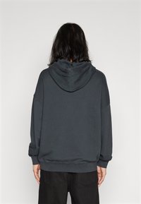 Dunkelgrauer, übergroßer Kapuzenpullover mit großer Kapuze, angeschnittenen Schultern, gerippten Bündchen und Saum. Weicher Stoff. Minimalistisches Design.
