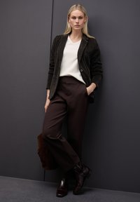 Tummanruskea corduroypikkutakki, vaalea V-neck-pusero, ruskeat housut ja kiiltävät ruskeat nilkkurit. Asusteina ruskea käsilaukku.
