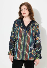 Blusa a maniche lunghe con sfondo blu navy scuro, decorata con motivi floreali e geometrici colorati, dettagli in pizzo e chiusura con bottoni.