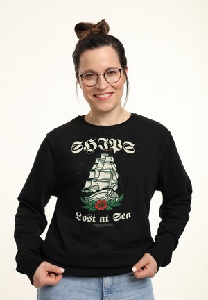Zwarte sweatshirt met een grafisch ontwerp van een schip en de tekst "SCHEDEN verloren op zee" en een rozenontwerp. Geribbelde halslijn en manchetten, casual pasvorm.