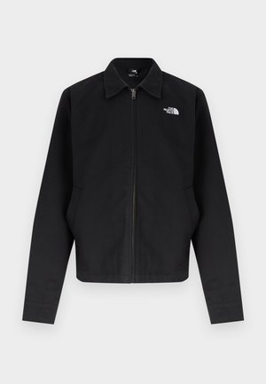 Crna jakna na patentni zatvarač s ovratnikom, dugim rukavima, bočnim džepovima i bijelim logotipom "The North Face" na lijevoj strani prsa.