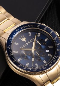Orologio in acciaio inossidabile dorato con quadrante blu navy, sotto quadranti e tachimetro. Presenta una finestra della data alle 4 e dettagli testurizzati.