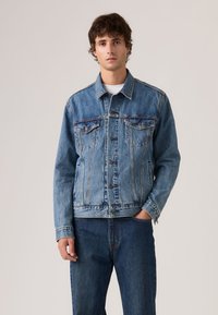 Μπλε τζιν μπουφάν με κλασική γραμμή, που διαθέτει δύο τσέπες στο στήθος, κλείσιμο με κουμπιά και αντίθετες ραφές. Φοριέται με μπλε τζιν παντελόνια.