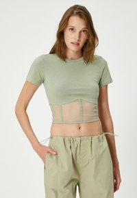Lys grøn cropped t-shirt med en tætsiddende top og mesh nederste panel, korte ærmer, rund udskæring, båret med lyse farvede trousers med snøre.