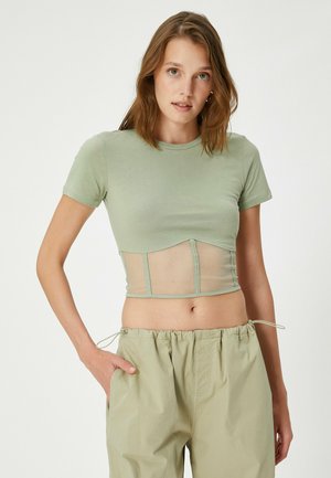 Lys grøn cropped t-shirt med en tætsiddende top og mesh nederste panel, korte ærmer, rund udskæring, båret med lyse farvede trousers med snøre.