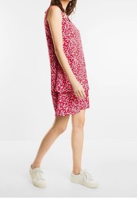 Rotes ärmelloses Kleid mit weißem Blumenmuster; lockere Passform, knielang, aus weichem Stoff; getragen mit weißen Sneakern.