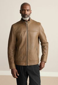 Jachetă din piele maro cu guler în picioare, fermoar frontal și două buzunare laterale; textură netedă și croială ajustată.