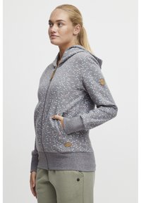 Grå zip-up hoodie med ljusblå och rosa prickar, kängurufickor, ribbade muddar och huva med snörning. Har en logotyp patch på ärmen.