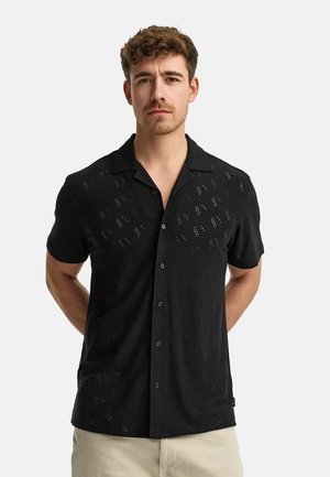 Black short-sleeve shirt made of textured fabric with diamond cut-out patterns and a relaxed collar. Front button closure and no pocket.