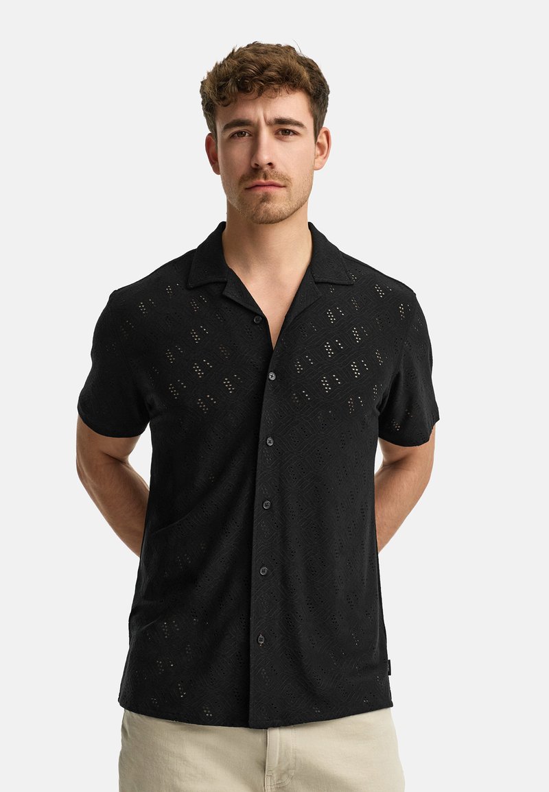 Black short-sleeve shirt made of textured fabric with diamond cut-out patterns and a relaxed collar. Front button closure and no pocket.