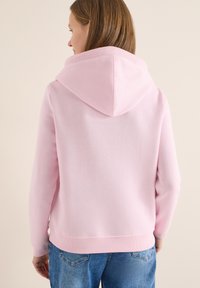 Sweat à capuche rose clair en tissu doux, avec une grande capuche pointue, des bords côtelés et une coupe décontractée, associé à un jean denim bleu.