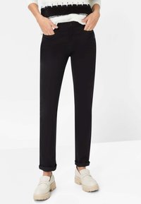 Zwarte, op maat gemaakte broek met een rechte snit, voorzien van steekzakken aan de voorkant en opgerolde pijpen. Gecombineerd met lichtgekleurde, chunky loafers.