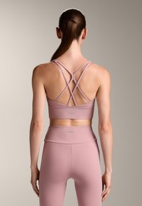 Ružové športové podprsenky s krížovými popruhmi, hladkou textúrou a detailom loga. Vhodné s zodpovedajúcimi legínami s vysokým pásom.