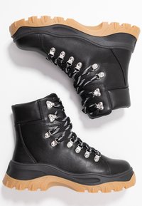 Černé kožené turistické boty mají stříbrné kovové detaily, černobílé tkaničky a silnou podrážku z gumy s hlubokým vzorkem.