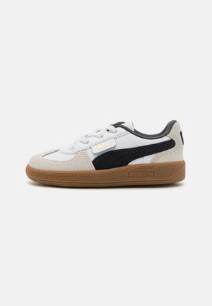 Sneaker bianche e nere con tomaia in suede e pelle, caratterizzate da una suola in gomma color caramello, design con lacci e accento del logo dorato.