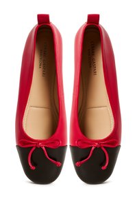Ballerine in pelle rossa con punta rotonda nera, caratterizzate da un fiocco e un tallone arcuato. L'interno è beige con dettagli di cucitura in vista.