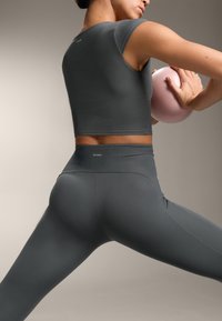 Top corto atletico a coste grigio scuro abbinato a leggings a vita alta, accompagnato da una palla da esercizio rosa, enfatizzando il design attillato e la texture.