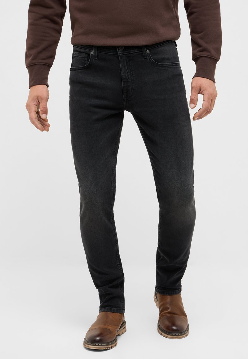 Czarne jeansy slim fit wykonane z denimu, z lekko wyblakłym wykończeniem. Połączone z brązowymi skórzanymi botkami sięgającymi kostki i brązowym swetrem.