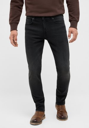 Schwarze, enganliegende Jeans aus Denim mit einem leicht verwaschenen Finish. Kombiniert mit braunen Leder-Stiefeletten und einem braunen Pullover.