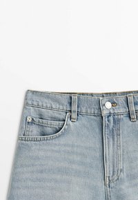 Jasnoniebieskie dżinsy wykonane z denimu mają dopasowany pas, dwie przednie kieszenie i metalowe okucia. Tkanina ma lekko chropowatą fakturę i efekt przetarcia.