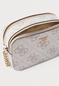 Beżowa torba tekstylna z tłoczonym wzorem logo, podwójnym zamkiem błyskawicznym i złotymi okuciami. Z boku ozdobiona łańcuszkiem.