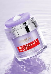 Bocal violet avec une bande argentée, étiqueté "L'Oréal Paris Revitalift Filler." Contient une goutte de crème blanche sur le couvercle, finition brillante.